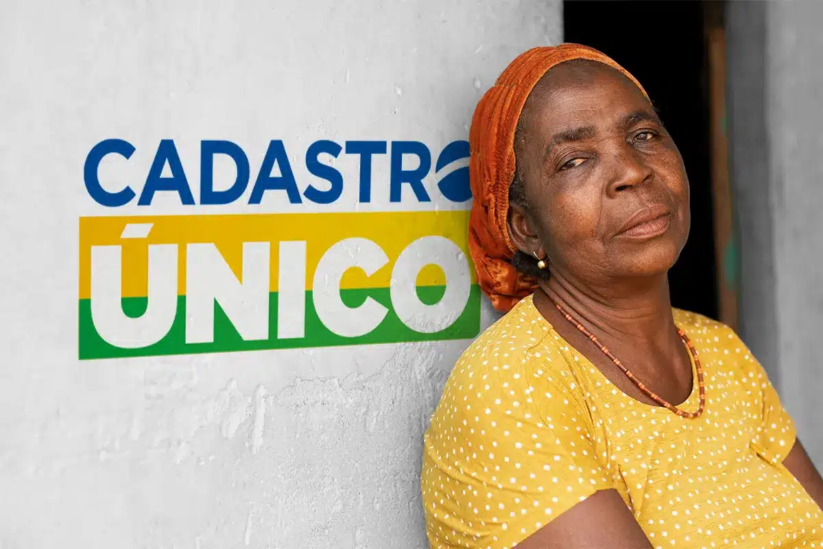 Mulher de lenço laranja e blusa amarela encostada em parede com logo do Cadastro Único ao fundo