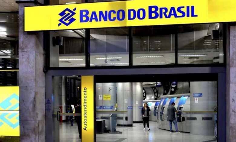Pessoas utilizando caixas eletrônicos em agência do Banco do Brasil iluminada à noite