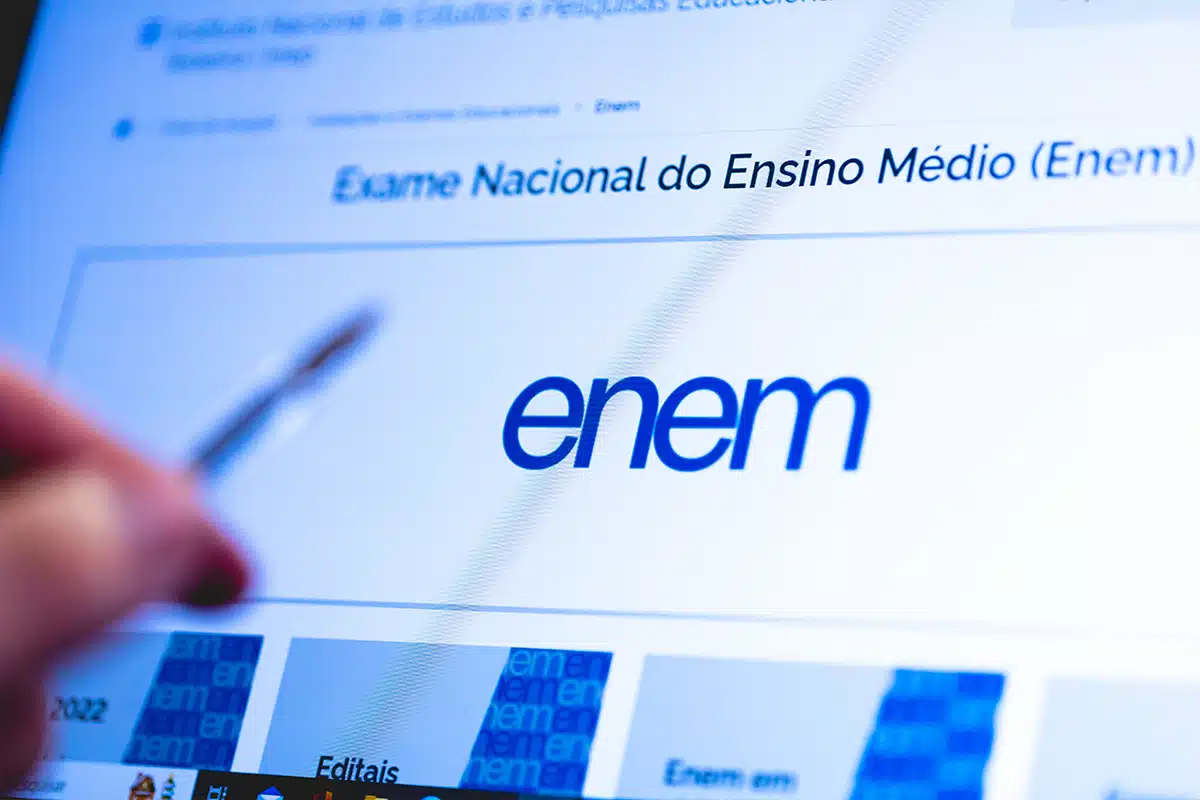 Tela do portal do Enem no Inep com logotipo azul em destaque e mão segurando caneta apontando para informações.